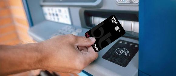 man holding a debit card ready to tap at an ATM